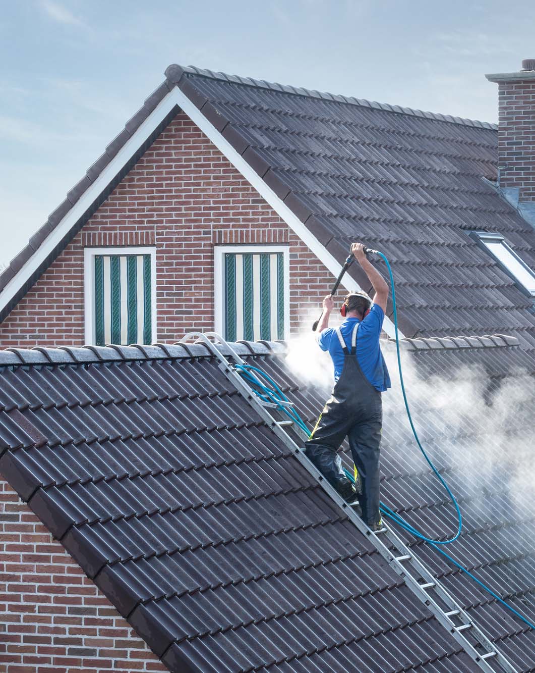 Cleaner with pressure washer at roof house cleaning roof tiles. Cleaner with pressure washer at roof of house cleaning the roof tiles, removing moss and weed cropped