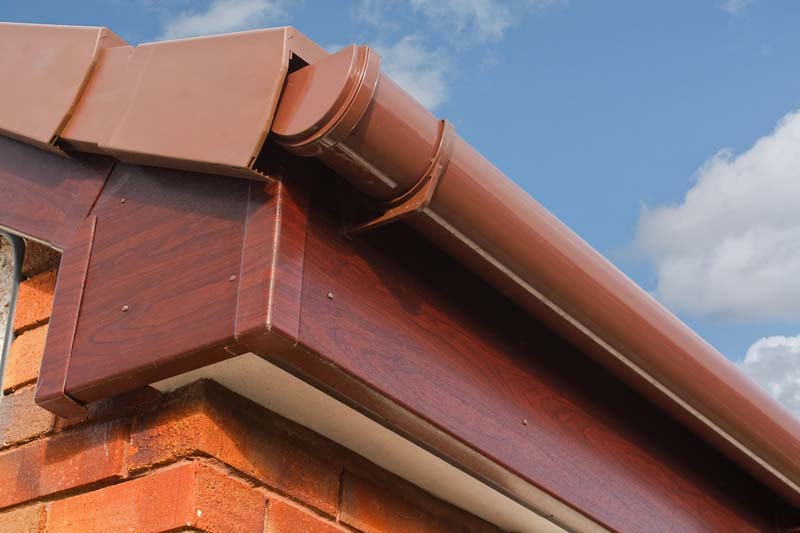 Roofline PVCU Soffit fascia board. Close up of Brown wood effect PVCu or plastic soffit, fascia and guttering on modern new build residential property